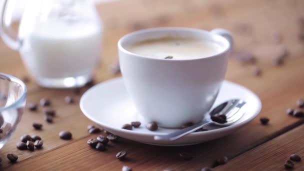 Taza de café y frijoles vertiendo a la mesa de madera — Vídeo de stock