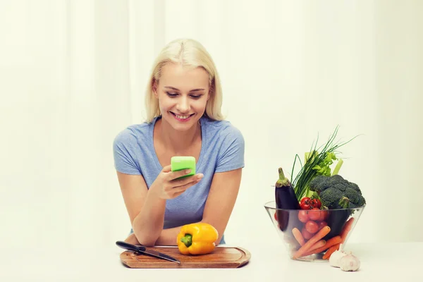 Mulher sorridente com smartphone cozinhar legumes — Fotografia de Stock