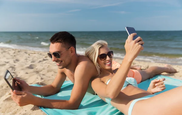 Lyckliga par med moderna prylar liggande på stranden — Stockfoto