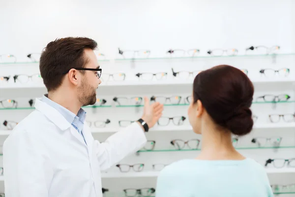 Mulher e óptico mostrando óculos na loja de óptica — Fotografia de Stock