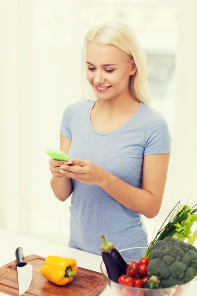 Mulher sorridente com smartphone cozinhar legumes — Fotografia de Stock