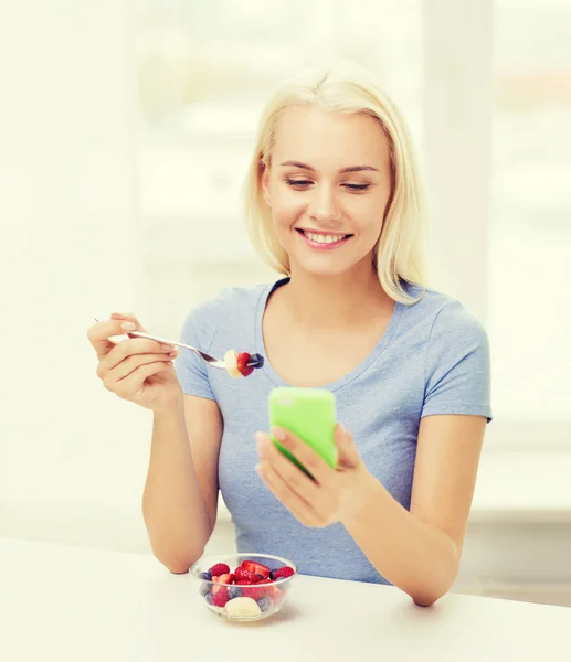 Kobieta z smartphone jedzenie owoców w domu — Zdjęcie stockowe
