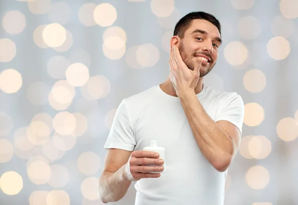 Felice giovane uomo applicando crema o lozione per il viso — Foto Stock