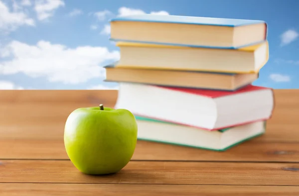 Närbild på böcker och grönt äpple på träbord — Stockfoto