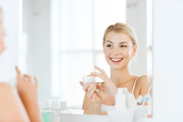 Happy woman applying cream to face at bathroom — Stock Photo, Image