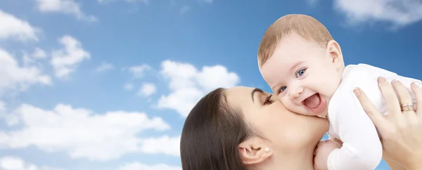Glückliche Mutter küsst ihr Baby über blauem Himmel lizenzfreie Stockbilder