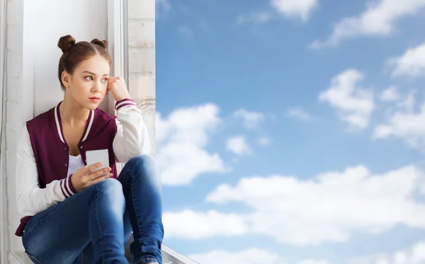 Девочка-подросток сидит на подоконнике со смартфоном — стоковое фото