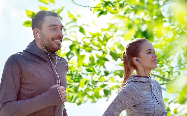 Happy couple with earphones running in city — Stock Photo, Image