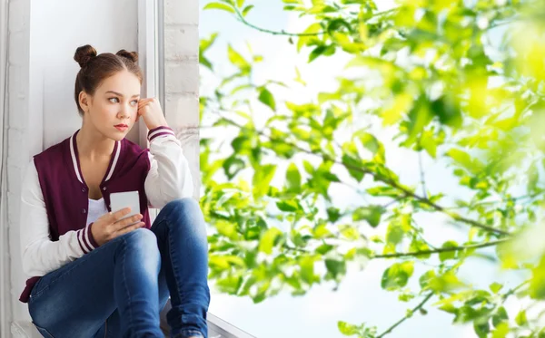 Девочка-подросток сидит на подоконнике со смартфоном — стоковое фото