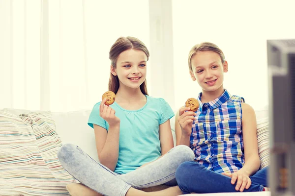 Ragazze felici guardando la tv e mangiare biscotti a casa — Foto Stock