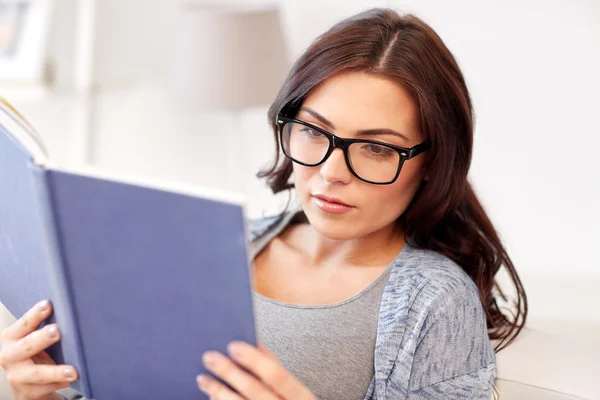 Mladá žena v brýlích čtení knihy doma — Stock fotografie
