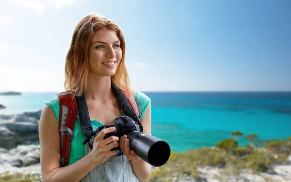 Счастливая женщина с рюкзаком и фотоаппаратом на берегу моря — стоковое фото