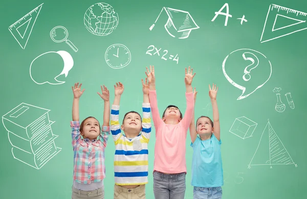 Happy children raising hands over green blackboard — 图库照片