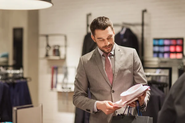 Happy young man choosing shirt in clothing store — Stock Photo, Image