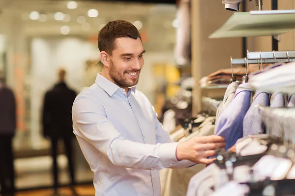 Happy young man choosing clothes in clothing store — Stock Photo, Image