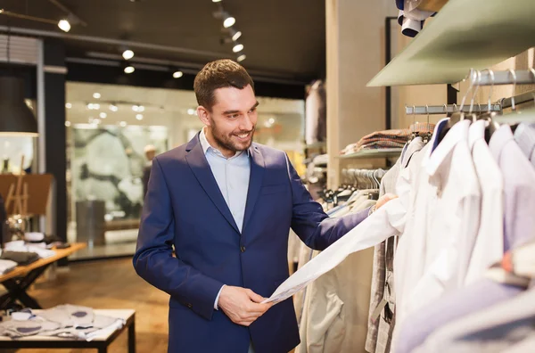 Happy young man choosing clothes in clothing store — Stock Photo, Image