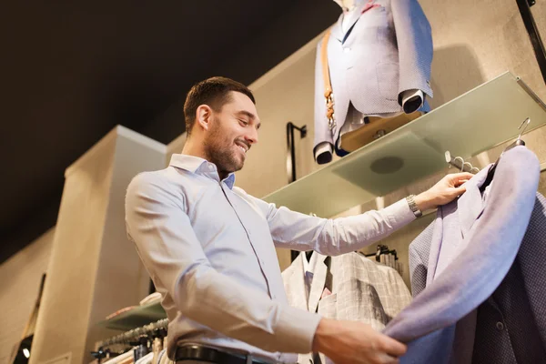 Happy young man choosing clothes in clothing store — Stock Photo, Image