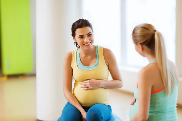 Twee gelukkige zwangere vrouwen zittend op ballen in sportschool — Stockfoto