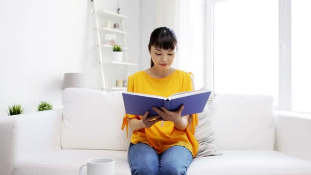 Smiling young asian woman reading book at home — Stock Video