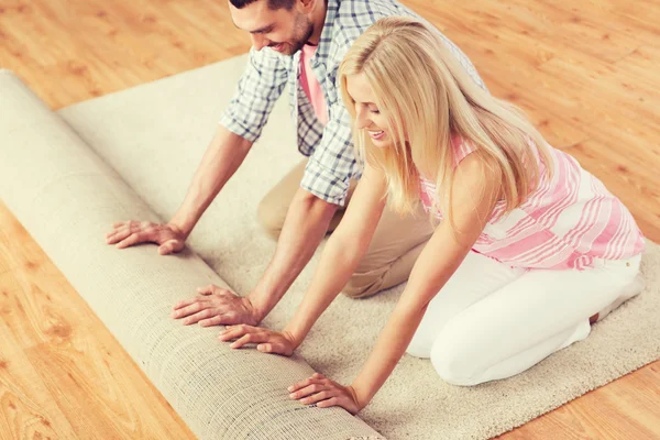 Casal feliz desenrolando tapete ou tapete em casa — Fotografia de Stock