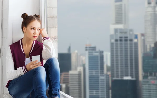 Tienermeisje zittend op de vensterbank met smartphone — Stockfoto