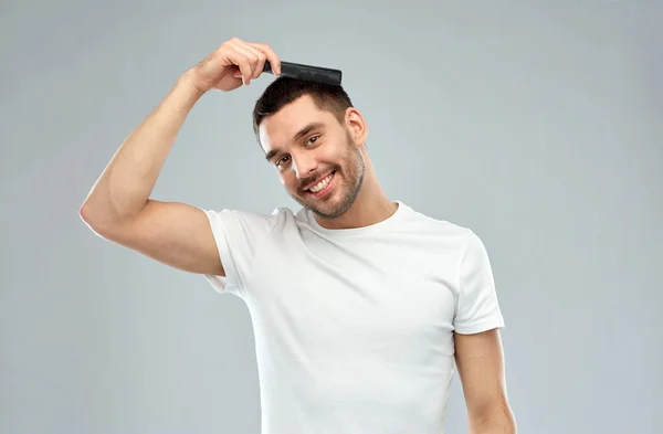 Homem feliz escovando o cabelo com pente sobre cinza — Fotografia de Stock