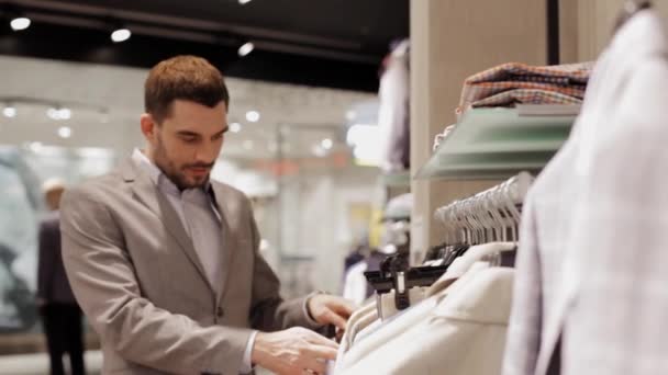 Gelukkig jonge man kiezen kleren in kledingwinkel — Stockvideo