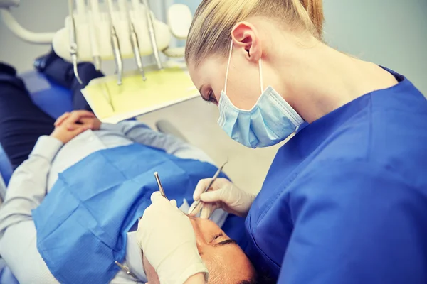 Dentista femenino en máscara chequeo de dientes de paciente masculino — Foto de Stock