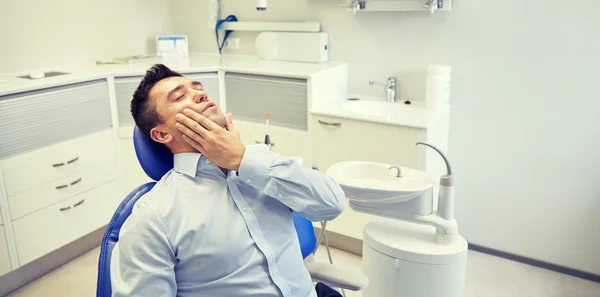 Мужчина, страдающий зубной болью и сидящий на стоматологическом стуле — стоковое фото