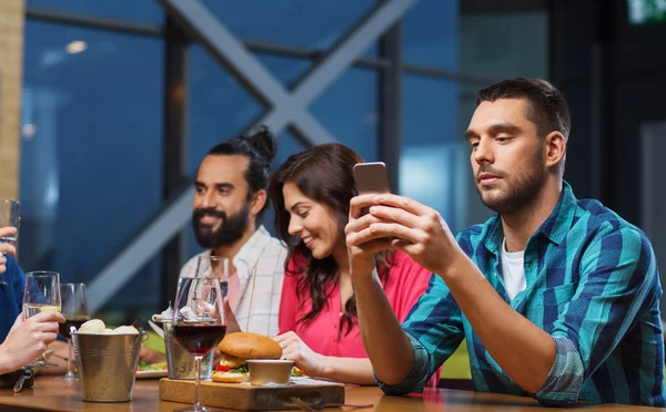 Man with smartphone and friends at restaurant — Stock Photo, Image