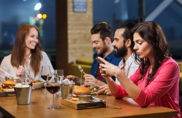 Vrouw met smartphone en vrienden op restaurant — Stockfoto