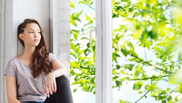 Triste chica adolescente bonita sentada en el alféizar de la ventana — Foto de Stock