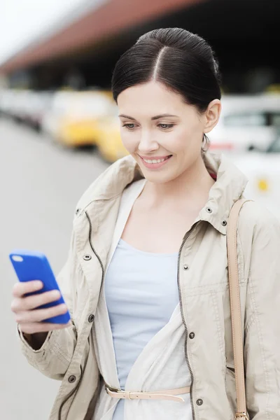 Usmívající se žena s smartphone za taxi v městě — Stock fotografie