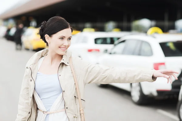 Jonge vrouw wuivende hand glimlachend en vangen taxi — Stockfoto