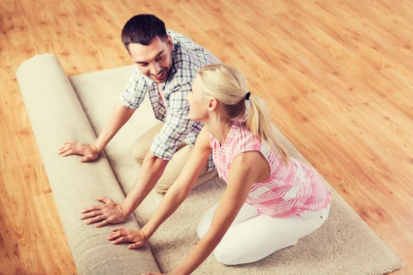 Casal feliz desenrolando tapete ou tapete em casa — Fotografia de Stock