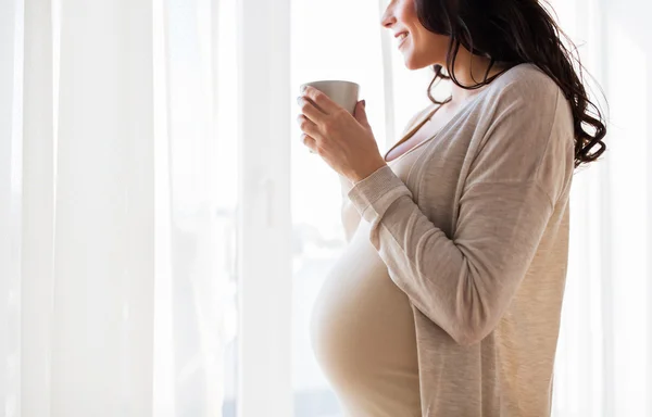 Close up of pregnant woman with tea cup at window — Stock Photo, Image