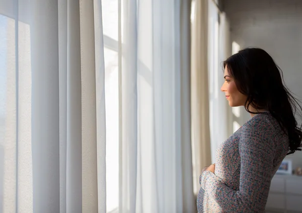 Nahaufnahme einer glücklichen Schwangeren, die zum Fenster blickt — Stockfoto