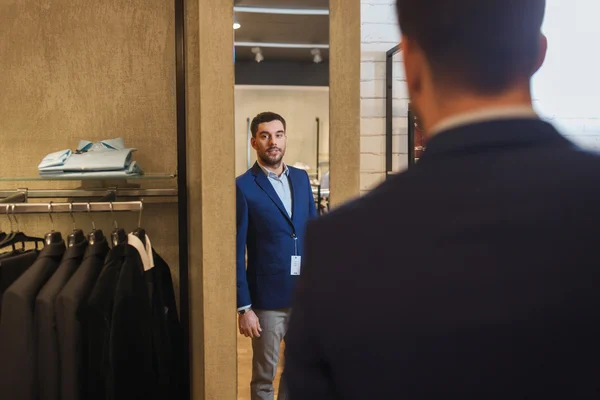 Man trying jacket on at mirror in clothing store — Stock Photo, Image