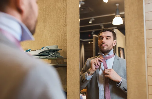 Hombre atando corbata en el espejo en tienda de ropa — Foto de Stock