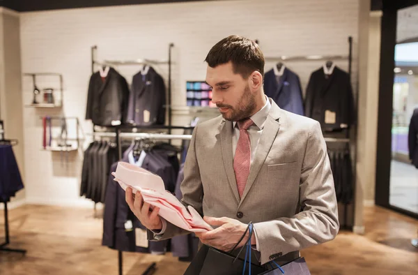 Man with bags choosing shirt in clothing store — Stock Photo, Image
