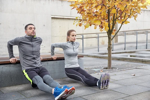 Couple doing triceps dip on city street bench — Stock Photo, Image