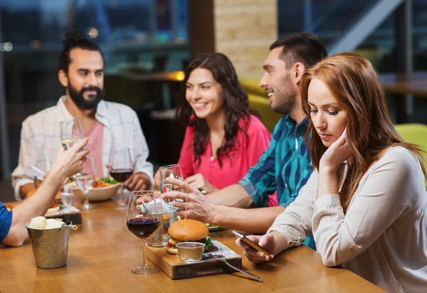 Žena s smartphone a přáteli v restauraci — Stock fotografie