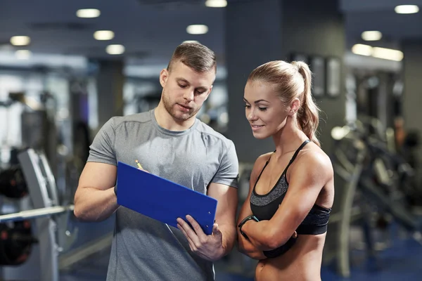 Spor salonunda kişisel antrenörüyle gülümseyen genç bir kadın. — Stok fotoğraf