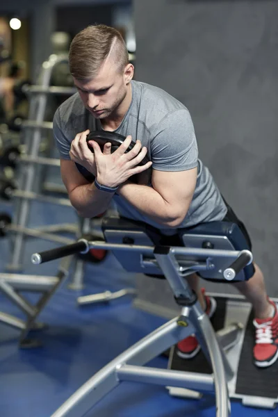 Ung man flexar tillbaka muskler på bänk i gym — Stockfoto