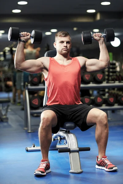 Joven con mancuernas flexionando los músculos en el gimnasio —  Fotos de Stock