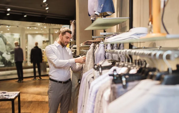 Glücklicher junger Mann wählt Kleidung im Bekleidungsgeschäft — Stockfoto
