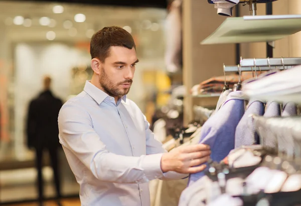 Happy young man choosing clothes in clothing store — Stock Photo, Image