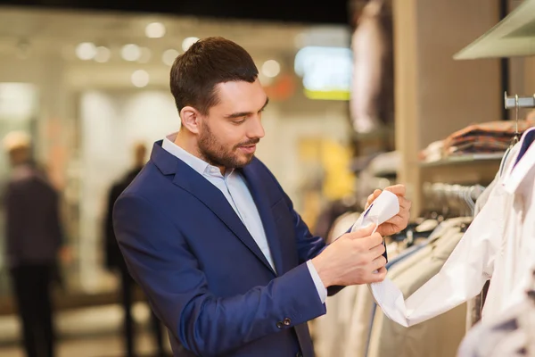 Happy young man choosing clothes in clothing store — Stock Photo, Image