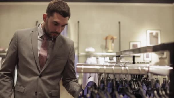 Giovane uomo che sceglie vestiti in negozio di abbigliamento — Video Stock