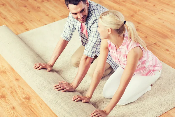 Feliz pareja desenrollando alfombra o alfombra en casa — Foto de Stock